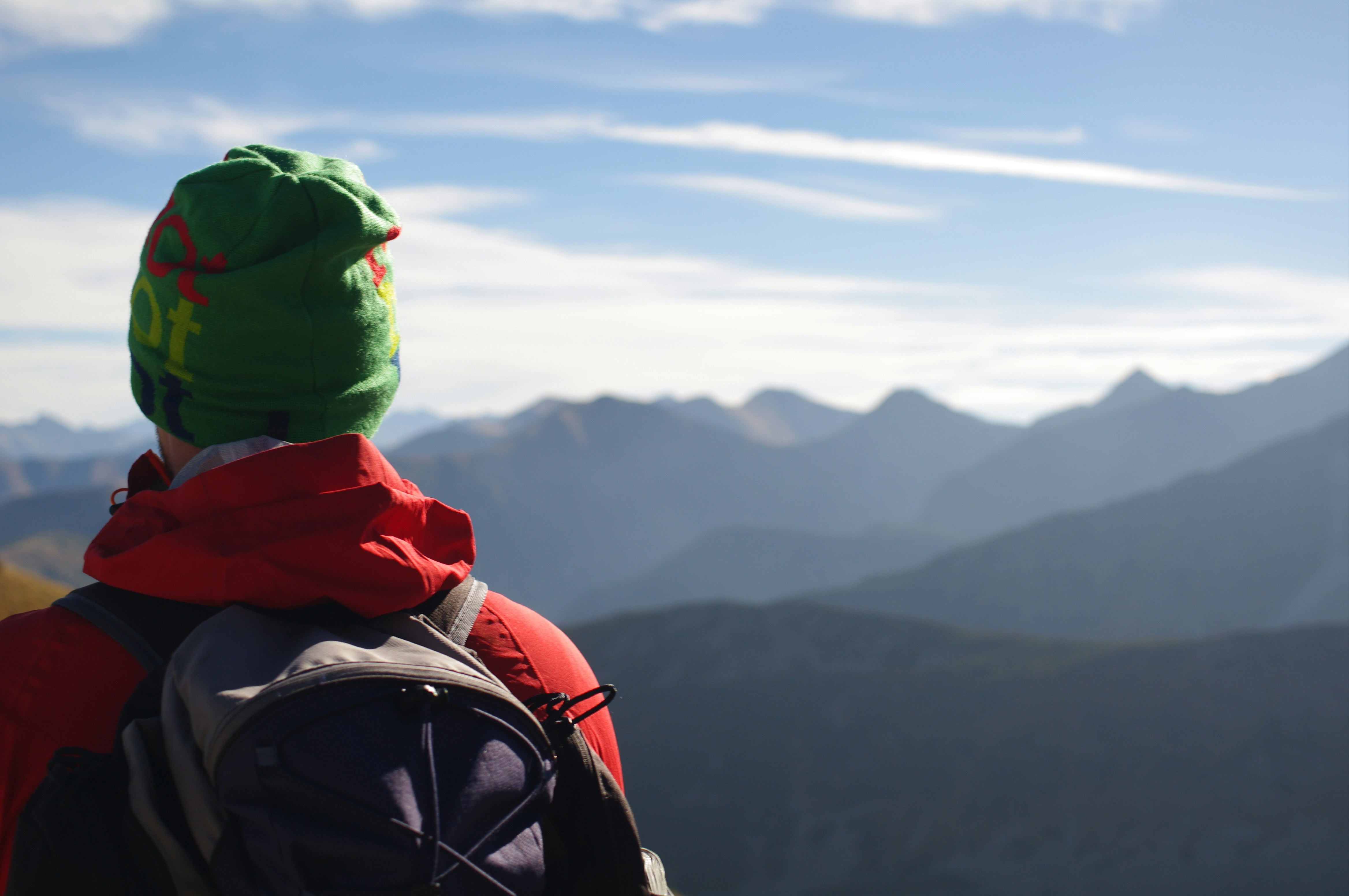 Un uomo con un cappello verde e una giacca rossa che guarda una catena montuosa