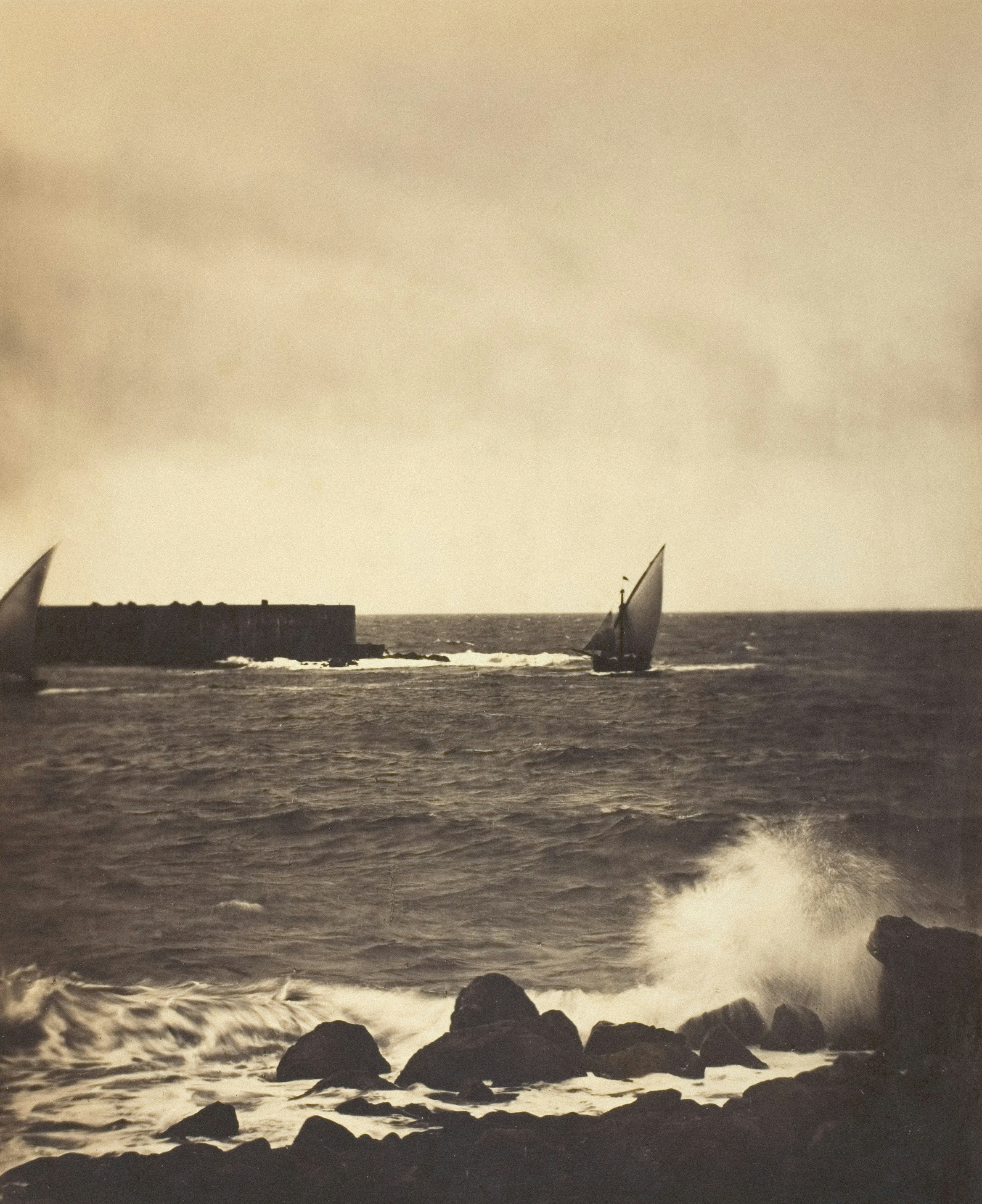 Sailboats navigate choppy waters near a rocky shore.