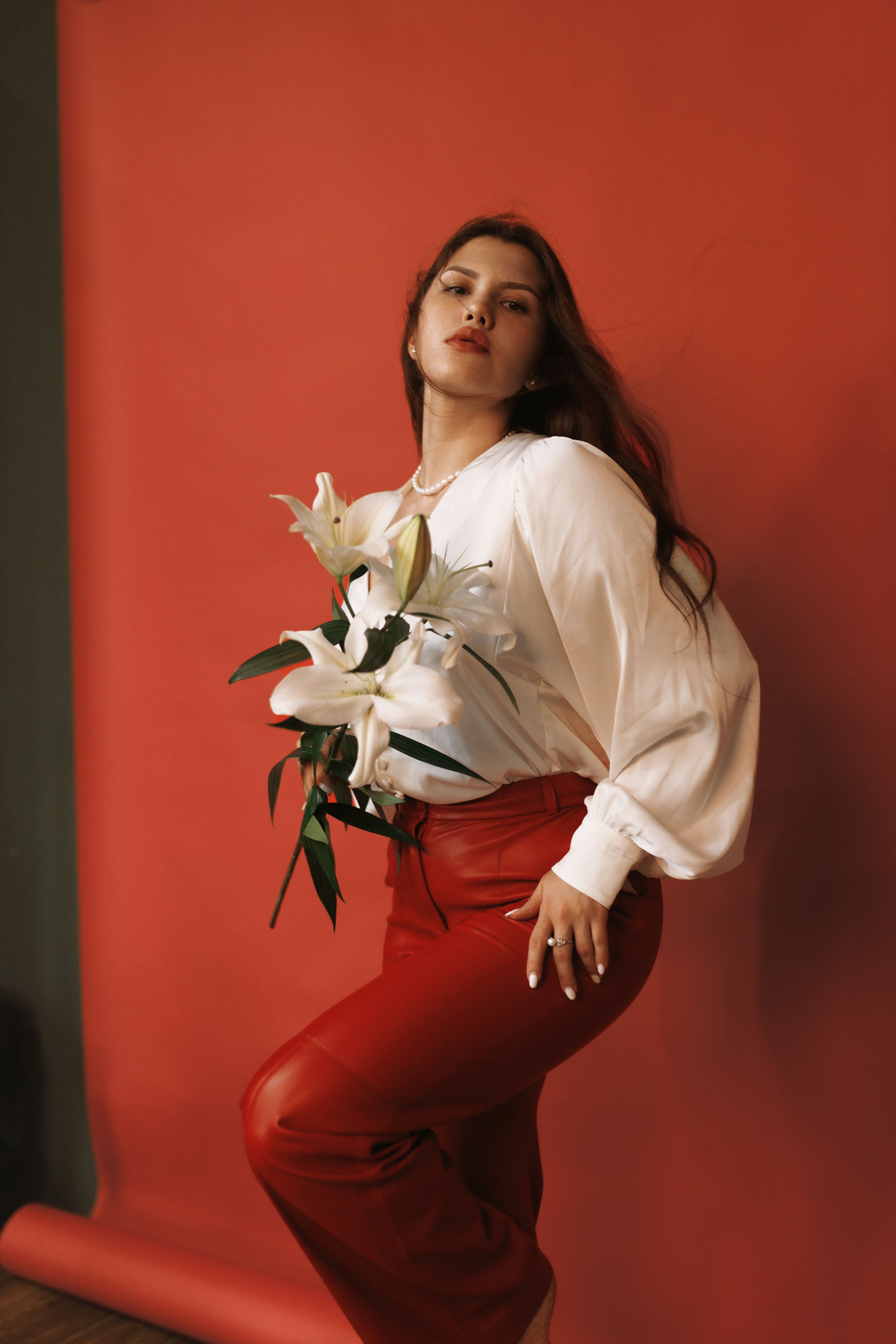 A woman leaning against a red wall holding a bouquet of flowers