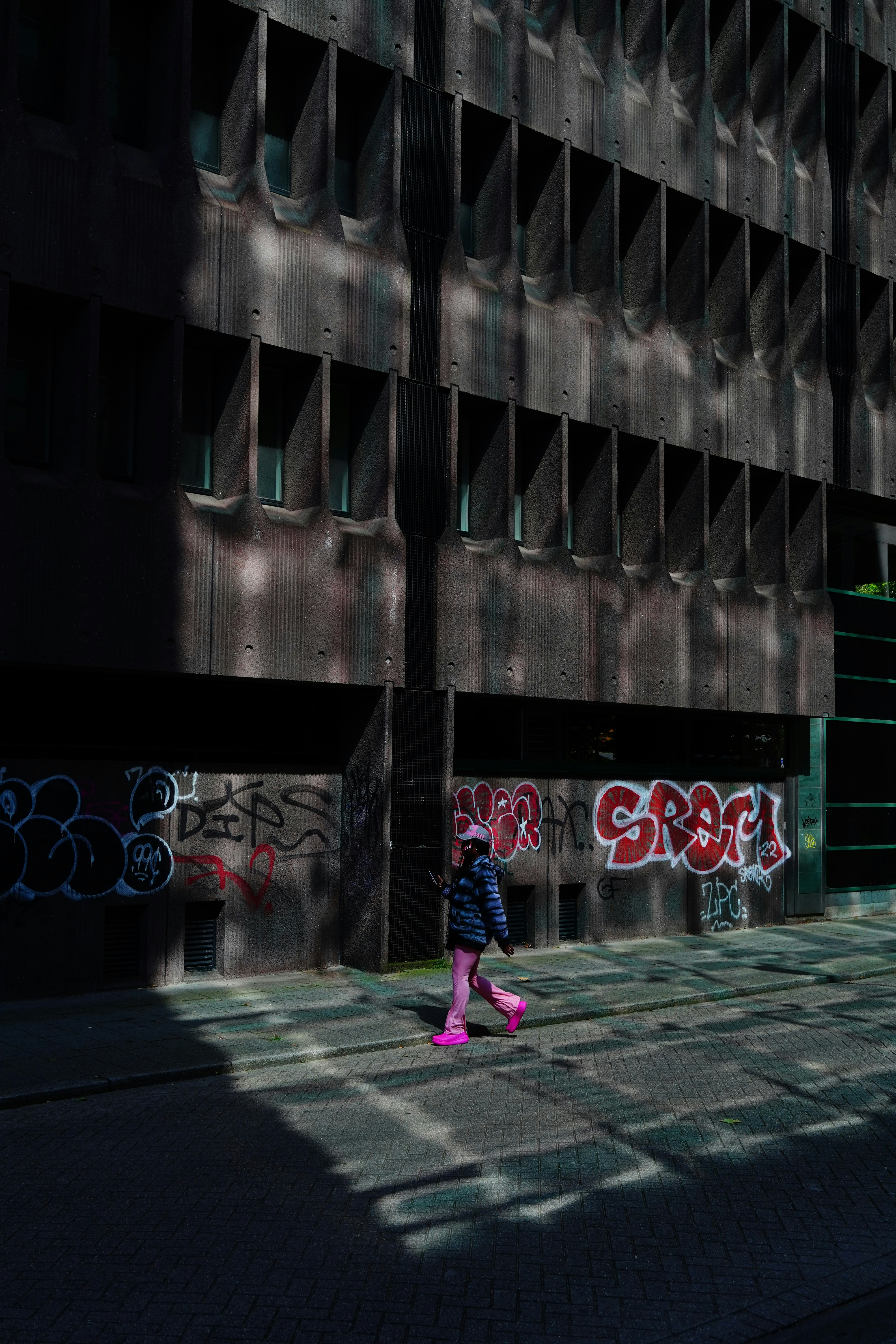 A woman walking down a street next to a tall building