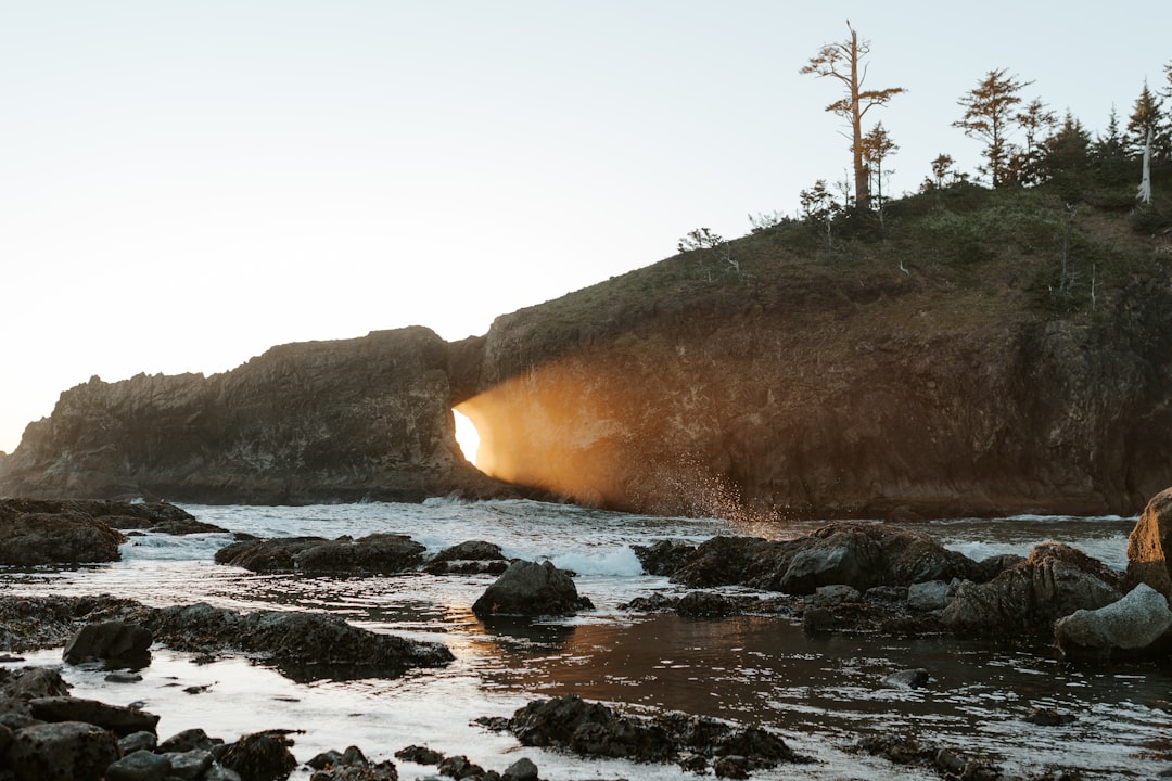 A person standing on a rocky beach next to a body of water, Sunset at Second Beach at Olympic National Park in Washingto
