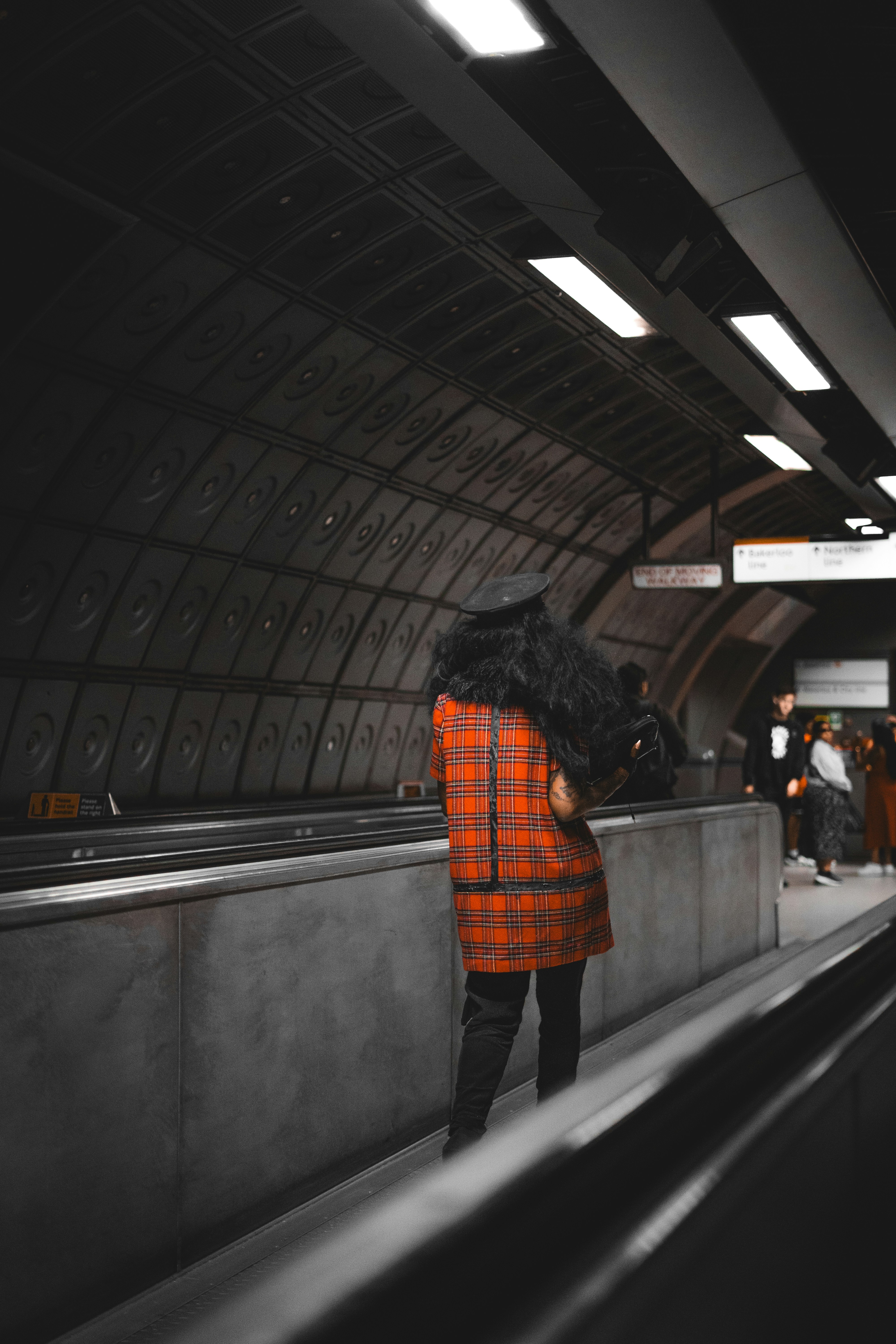 A woman in an orange coat is standing on a subway platform