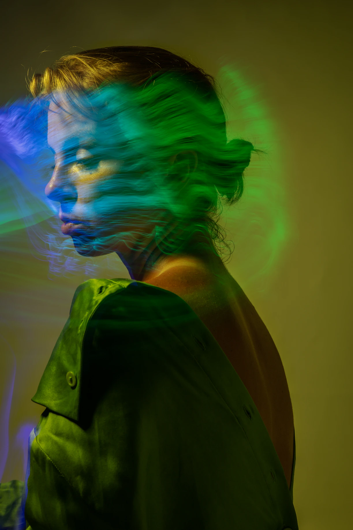 A woman with green and blue hair standing in front of a wall