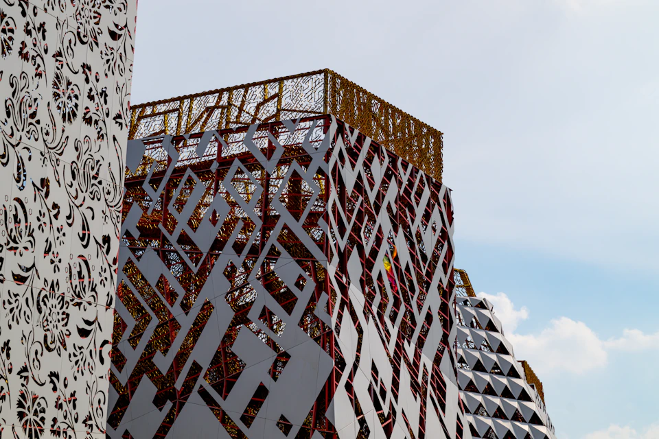The image shows a modern architectural structure with a unique design featuring a grid-like pattern on its facade, composed of white and red panels. The building is situated against a clear blue sky, creating a striking contrast between the man-made structure and the natural environment.