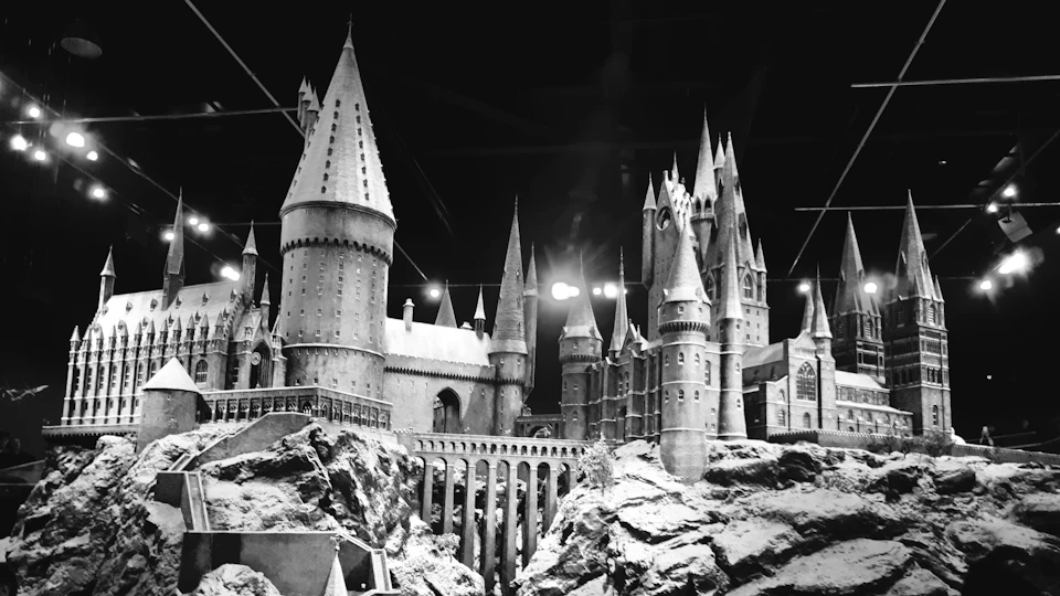 The image presents a meticulously crafted replica of the Hogwarts Castle, a popular landmark from the Harry Potter series. The castle is constructed entirely out of white sand and features multiple towers and spires that reach towards the night sky. The castle's intricate details are highlighted against a black background, making it stand out prominently in the scene.
