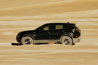 A black car driving through a sandy area