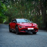 A red car driving down a street next to trees