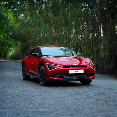 A red car driving down a street next to trees