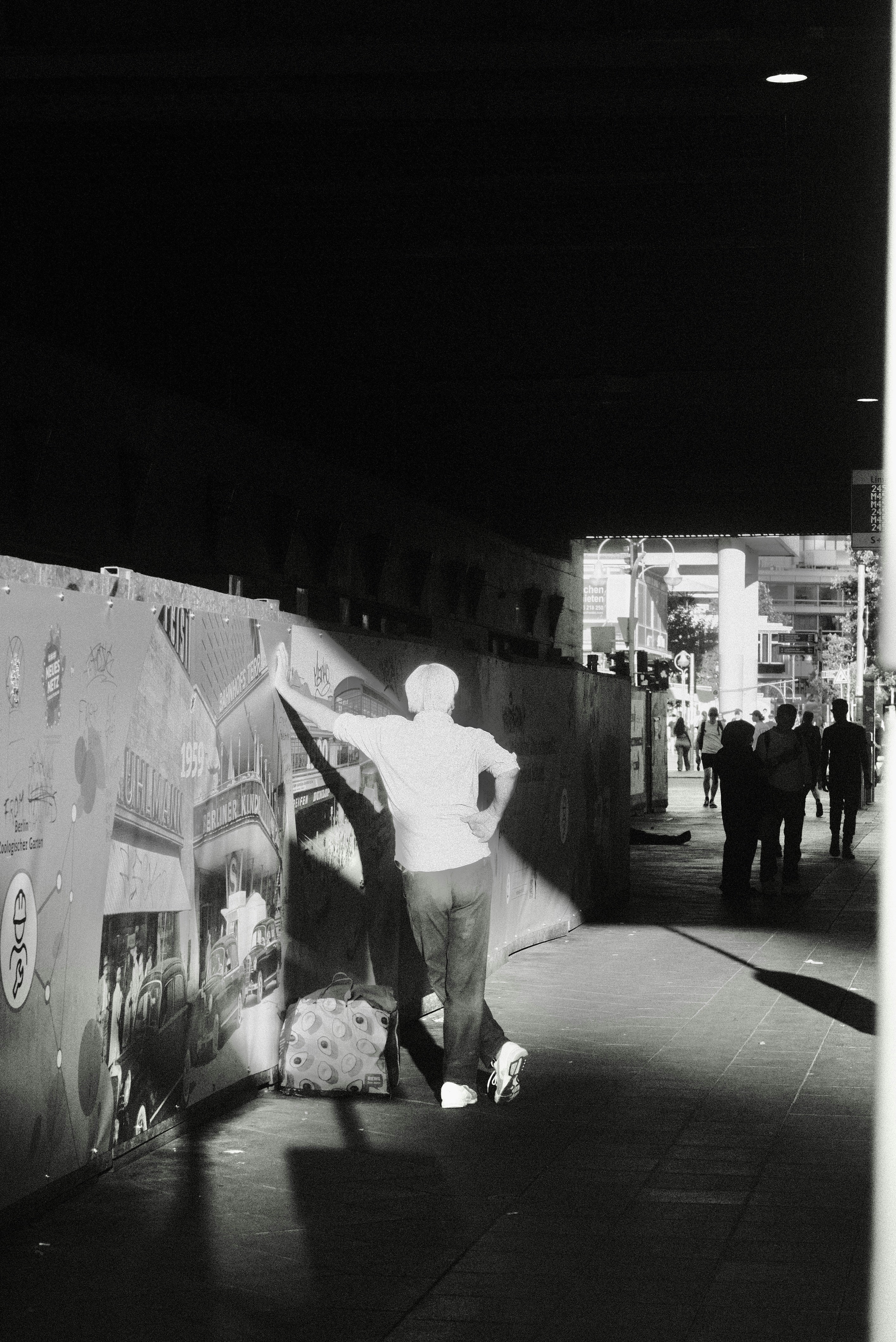 A black and white photo of a man standing next to a wall
