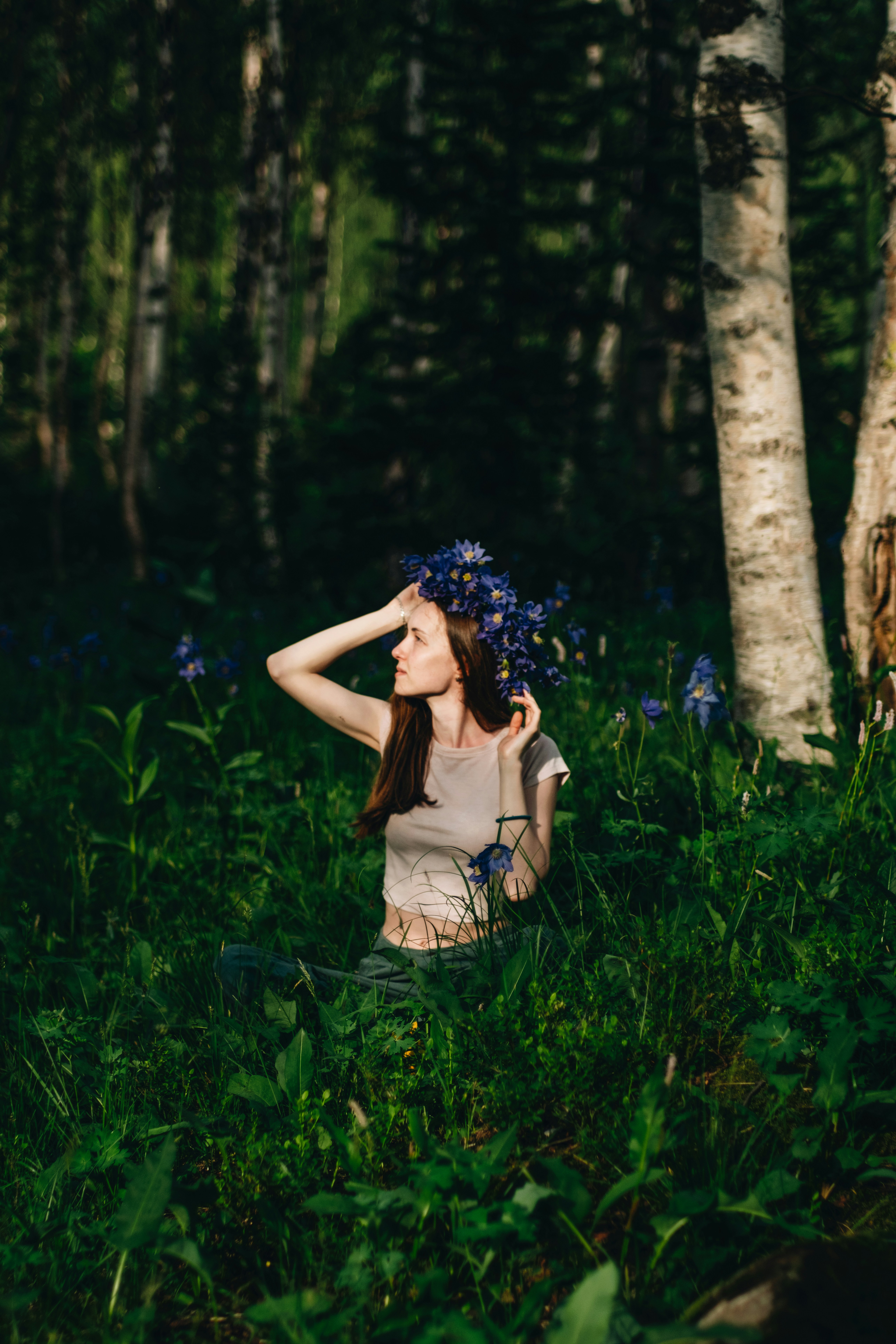 A woman standing in a forest with a blue flower in her hair