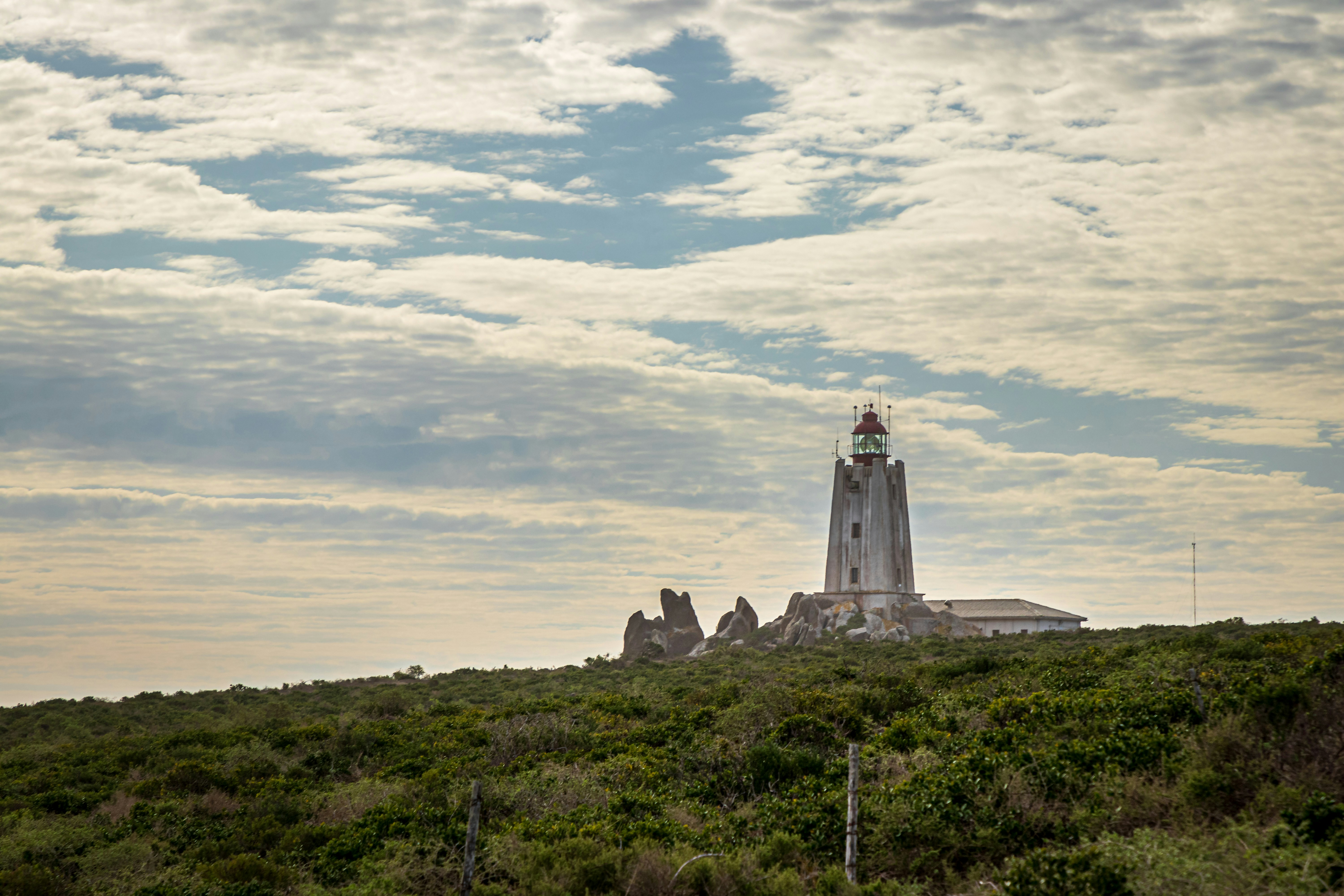 A lighthouse on top of a hill under a cloudy sky