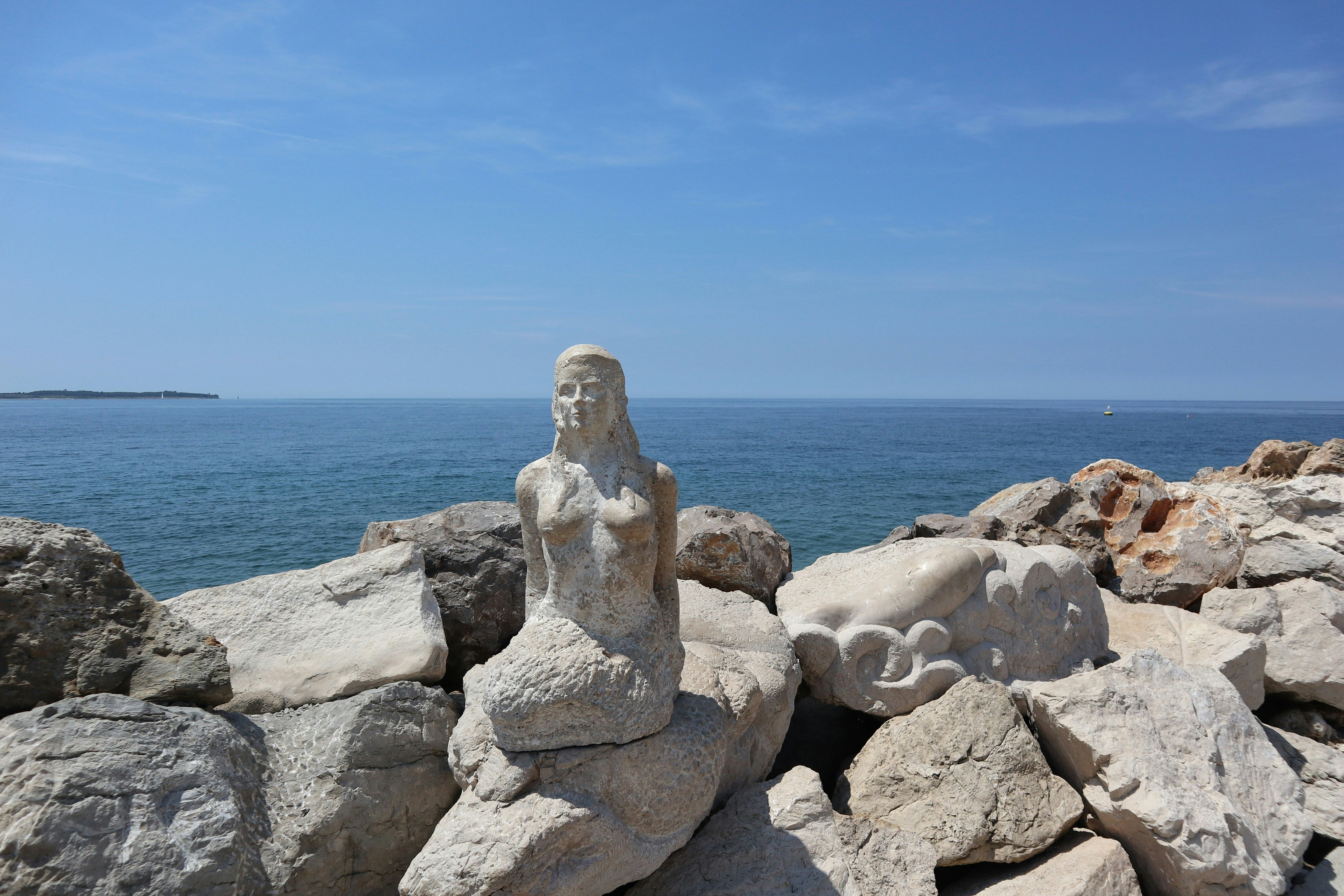 A statue sitting on top of a pile of rocks next to the ocean, 
