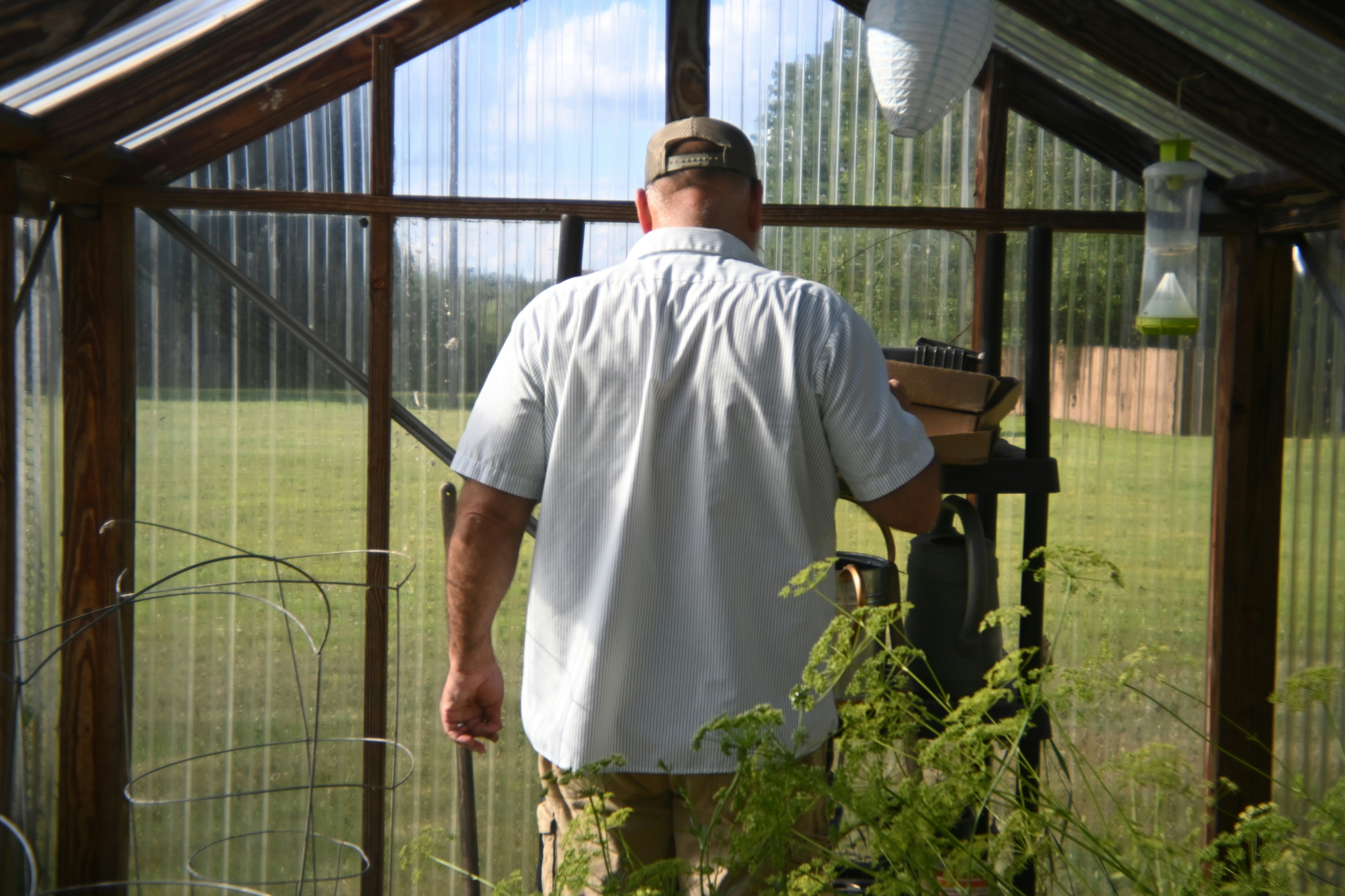 A man in a white shirt and khaki pants standing in a greenhouse