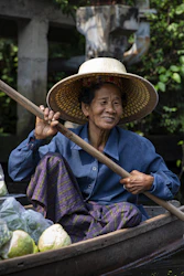 A woman in a hat rowing a boat filled with vegetables