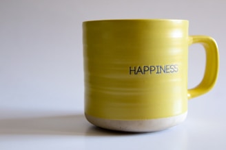 A yellow coffee mug with the words happiness written on it