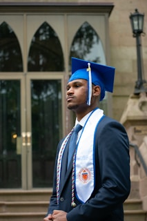 A man in a graduation cap and gown standing in front of a building