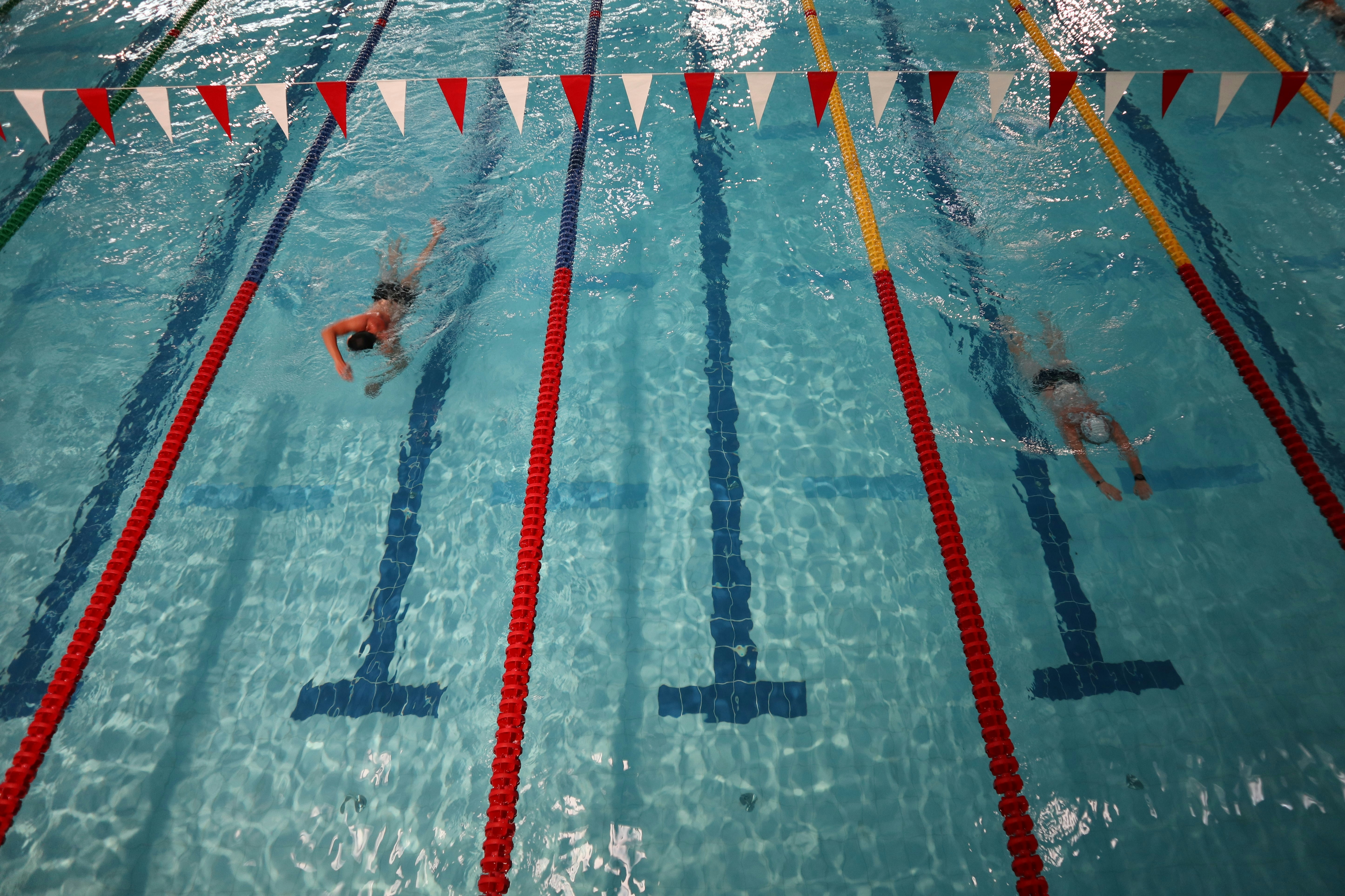 Mid-distance swimmer in competition pool lane, dark blue water, dramatic sports photography
