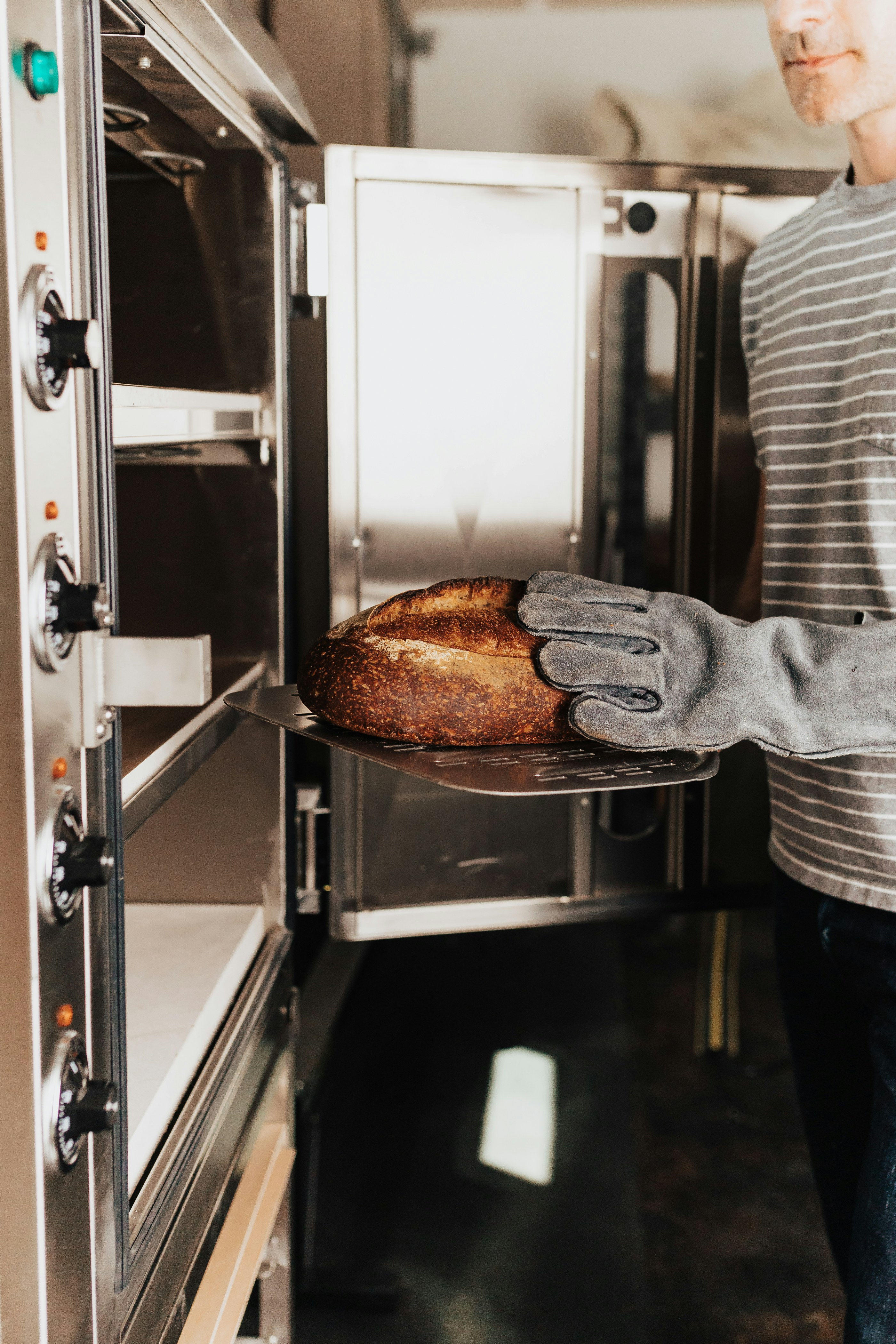 A man holding a loaf of bread in front of an oven