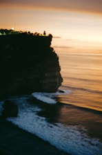 A sunset view of the ocean with a cliff in the foreground