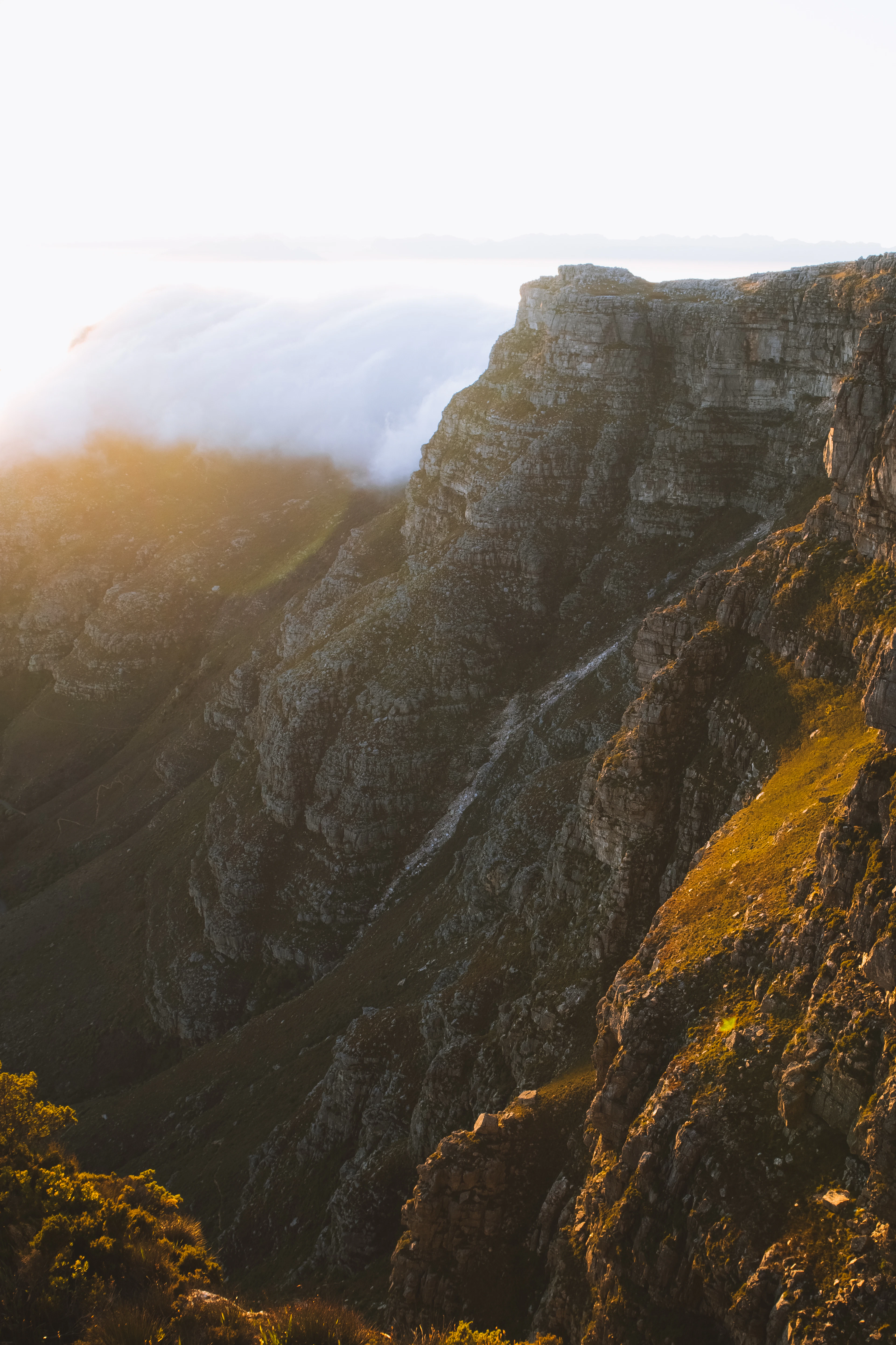 Close view of Table Mountain's cliffs with its cloud 'tablecloth' spilling over the summit at sunset.