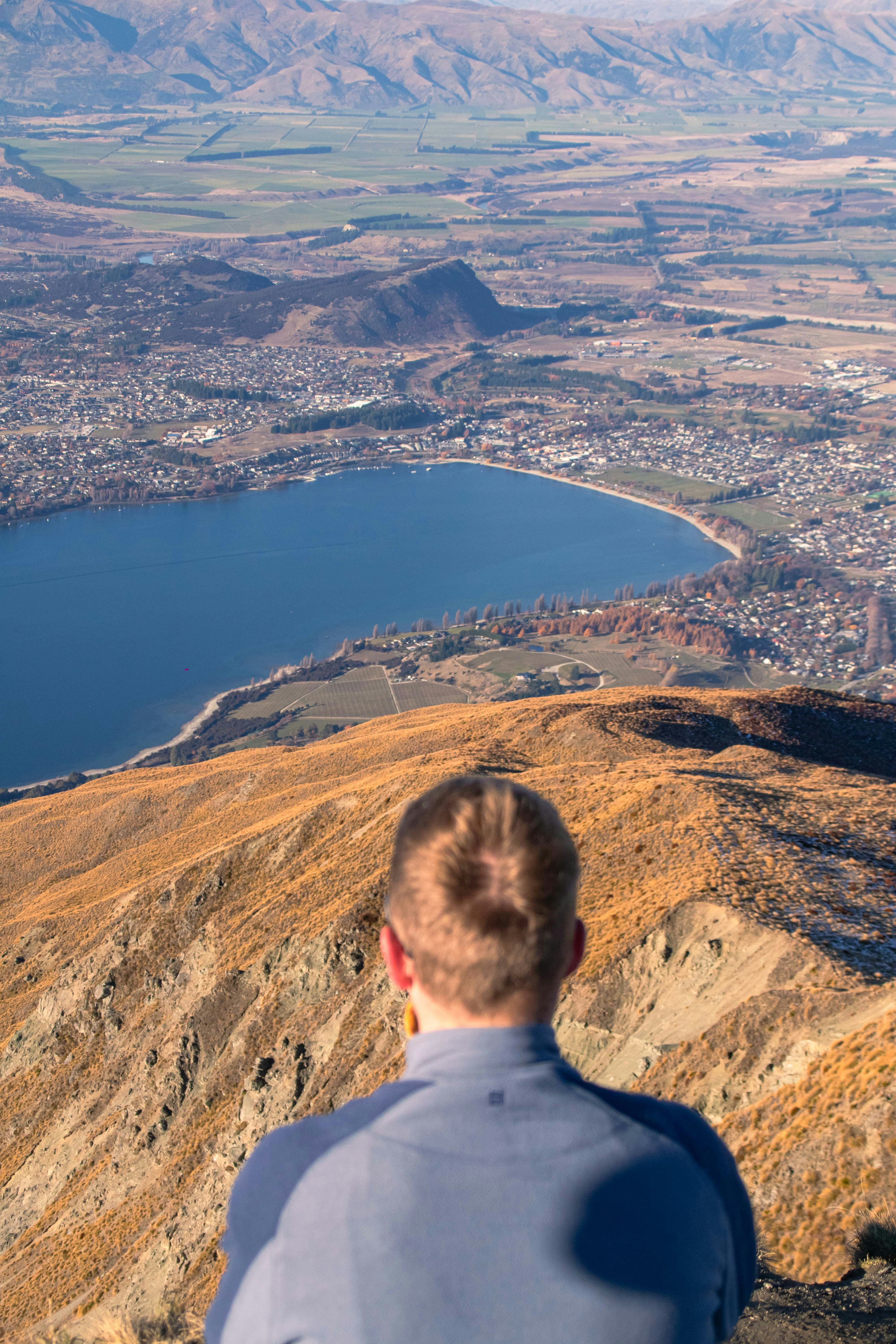 A man sitting on top of a mountain overlooking a city