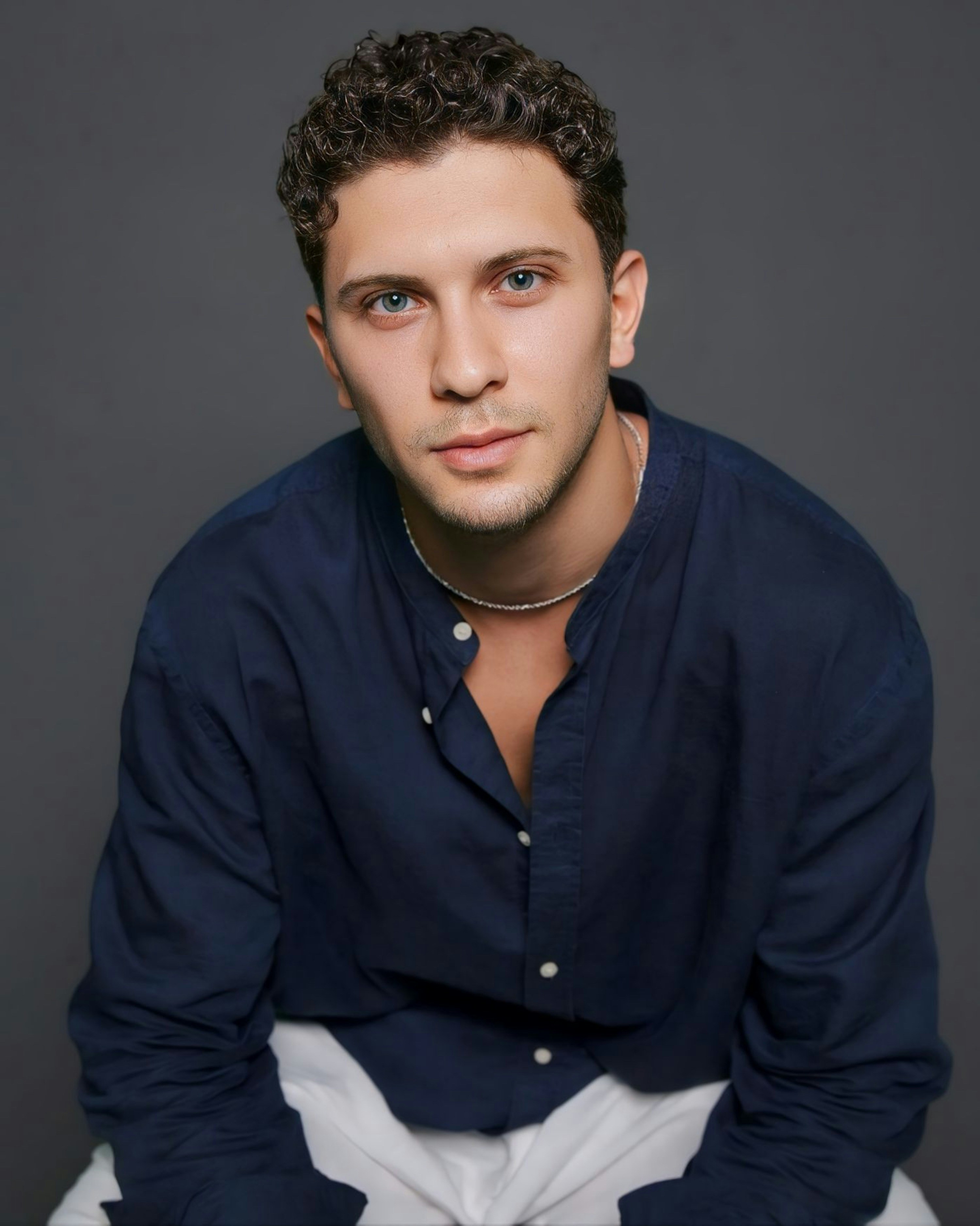 A man sitting on top of a bed wearing a blue shirt