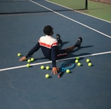 A man laying on a tennis court surrounded by tennis balls