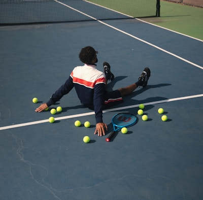 A man laying on a tennis court surrounded by tennis balls
