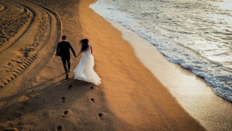 A bride and groom walking on the beach