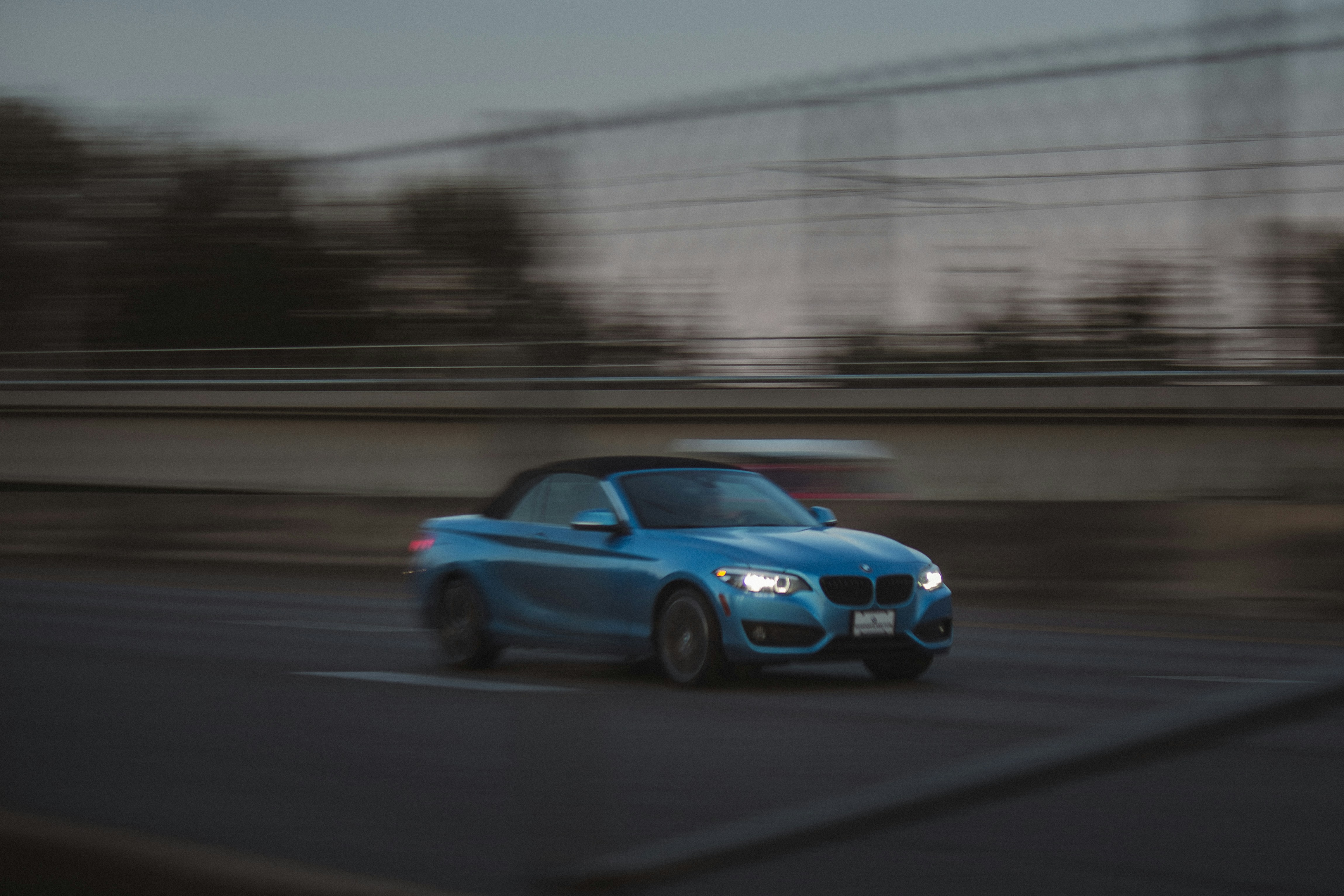 A blue car driving down a street next to a bridge