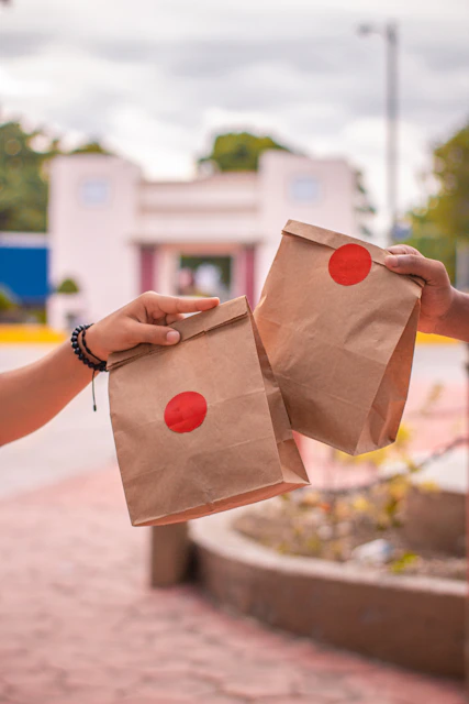 Two people holding brown paper bags with red polka dots