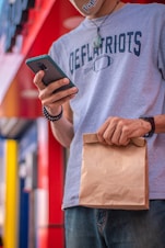 A man holding a brown paper bag and a cell phone