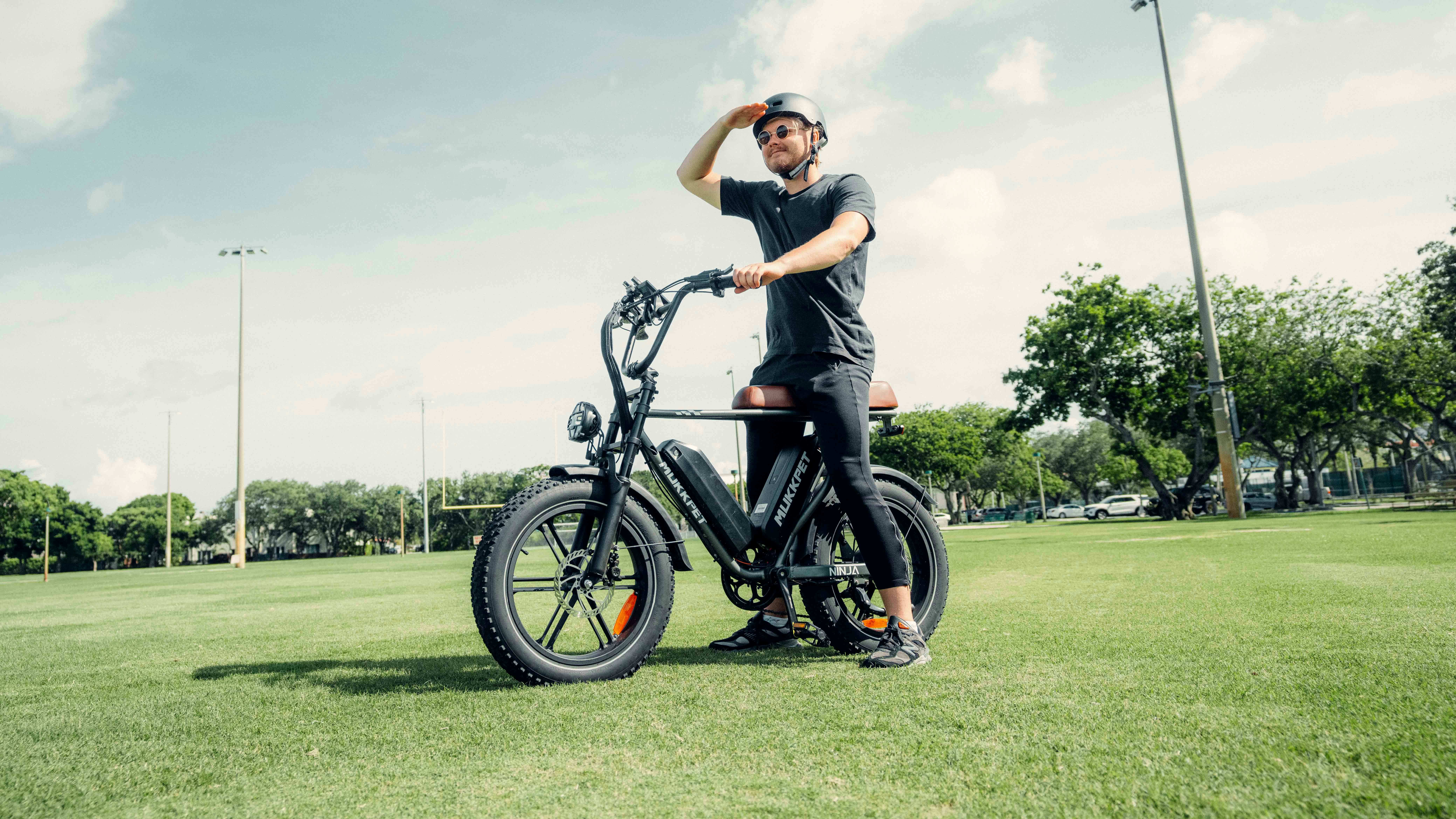 A man standing next to a bike on a lush green field