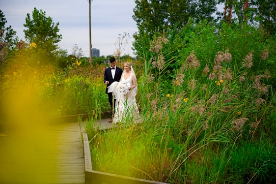 A bride and groom walking through tall grass