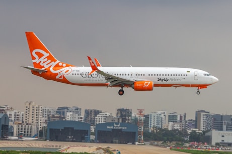 An orange and white jet airliner flying over a city