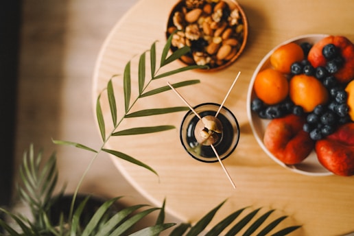 A wooden table topped with a bowl of fruit and a plate of nuts