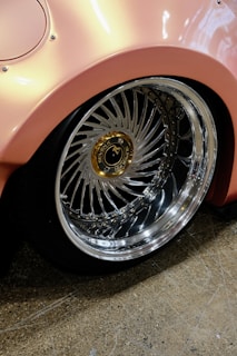 A pink car with chrome rims parked in a garage