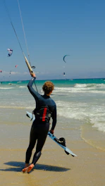 A man in a wet suit holding onto a kite on the beach
