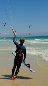 A man in a wet suit holding onto a kite on the beach