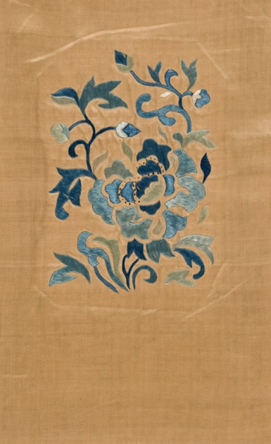 Blue floral embroidery on tan silk background — a textile tradition that runs through the DNA of Chinese-style embroidered accessories.