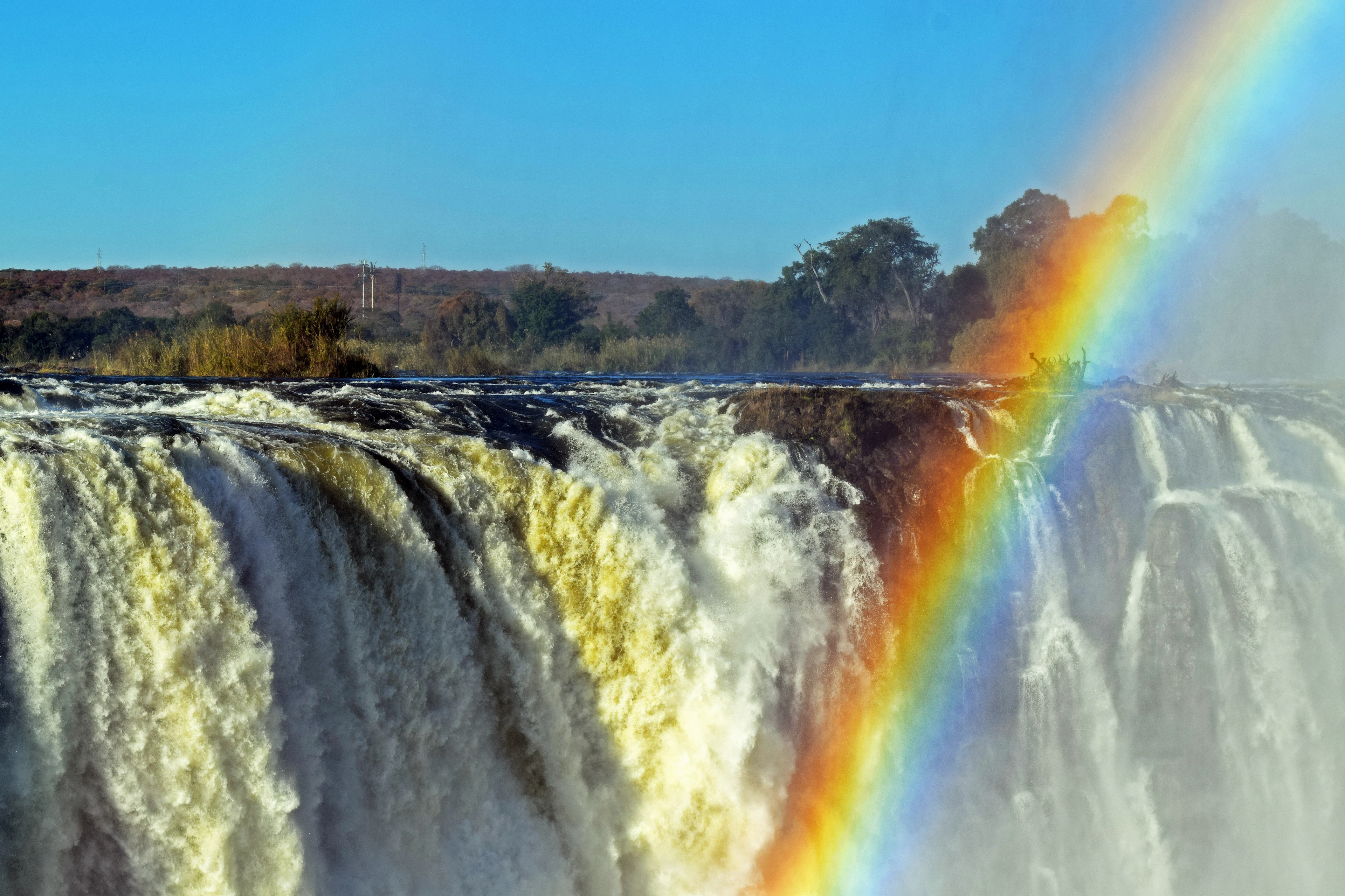 A rainbow arcing through the spray at the lip of Victoria Falls as the Zambezi pours over the basalt edge.