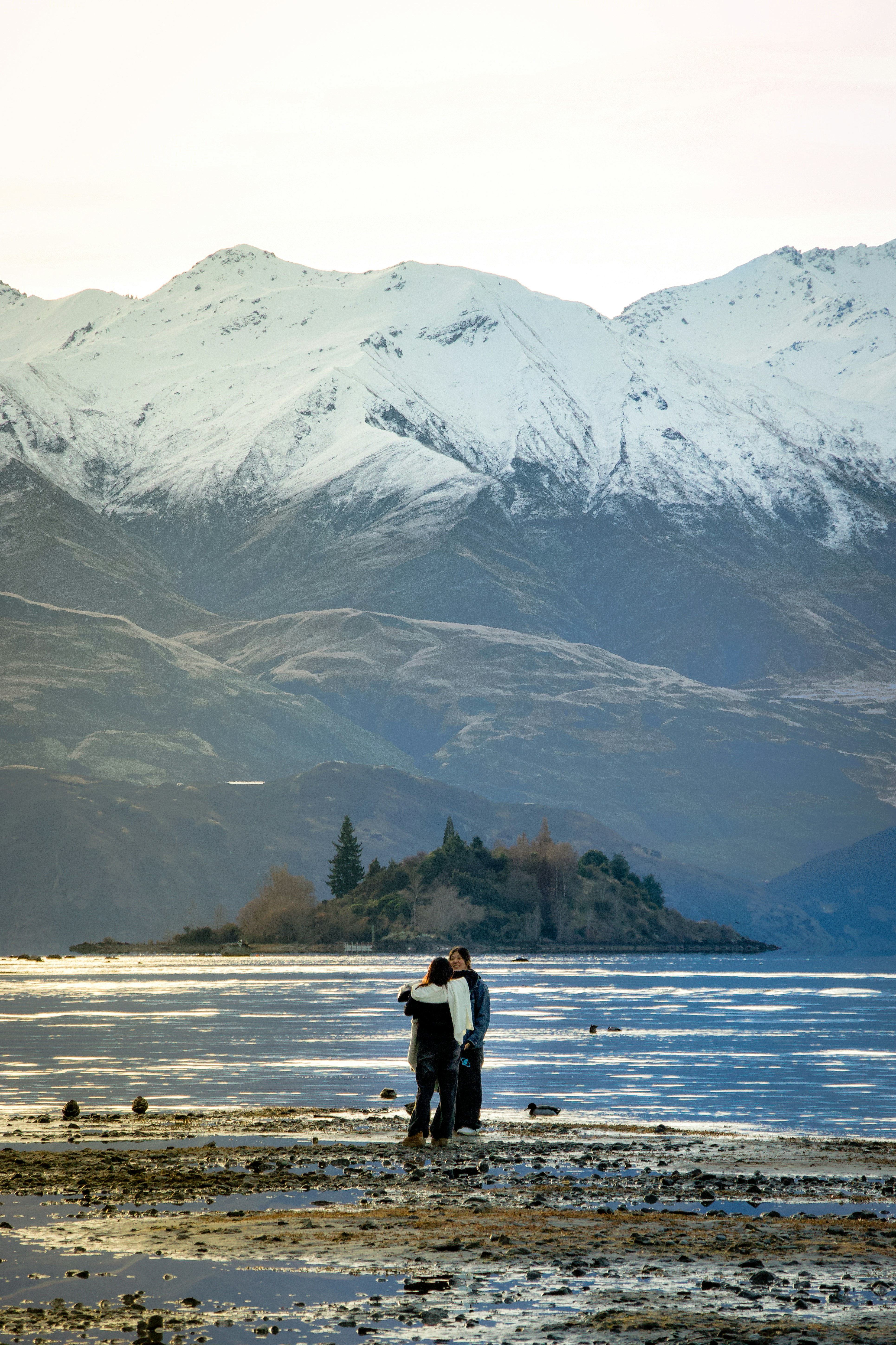 Two people standing on a beach with mountains in the background