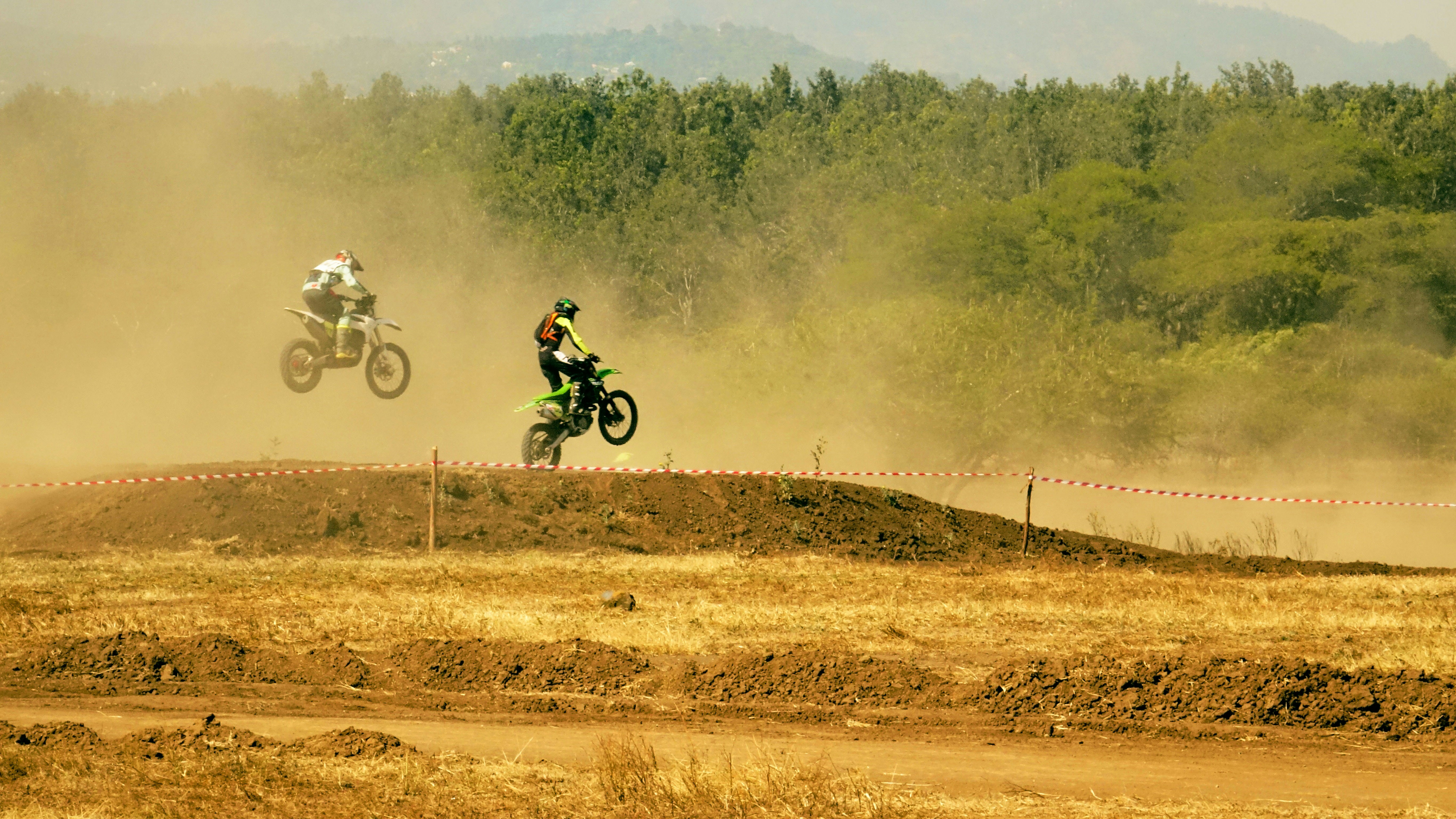 Honda dirt bike jumping over hill in off-road terrain, dust clouds, action shot