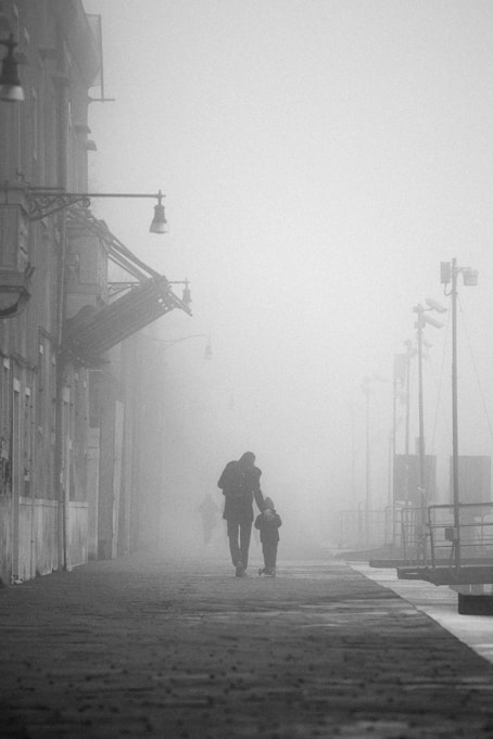 A couple of people walking down a street in the fog