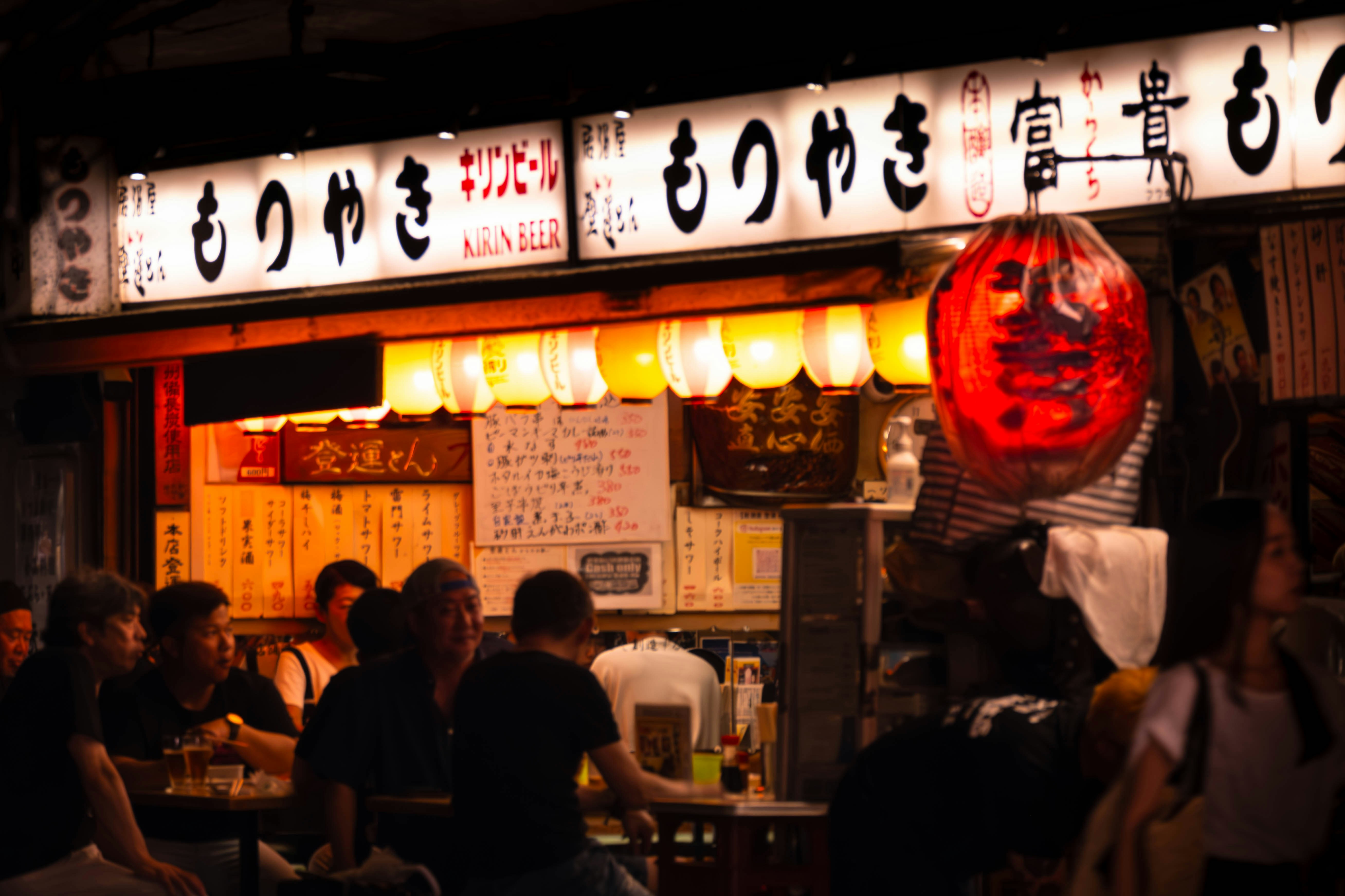 A group of people standing outside of a restaurant, outdoor traditional Japanese bar under the railway