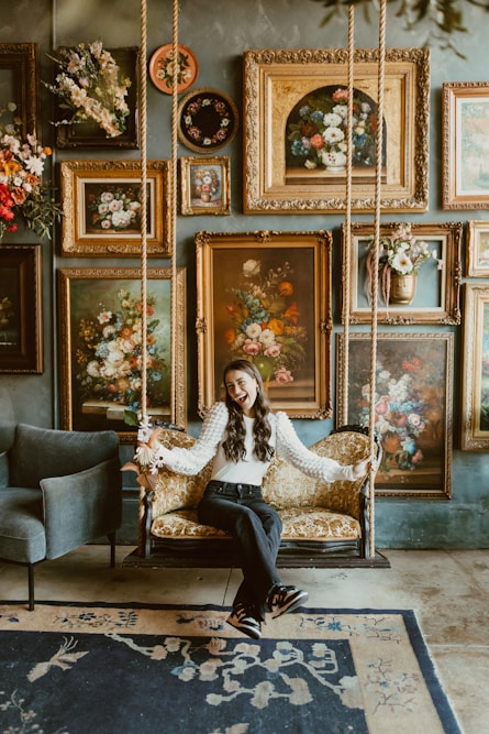 A woman sitting on a swing in a room filled with paintings