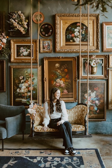 A woman sitting on a swing in a room filled with paintings