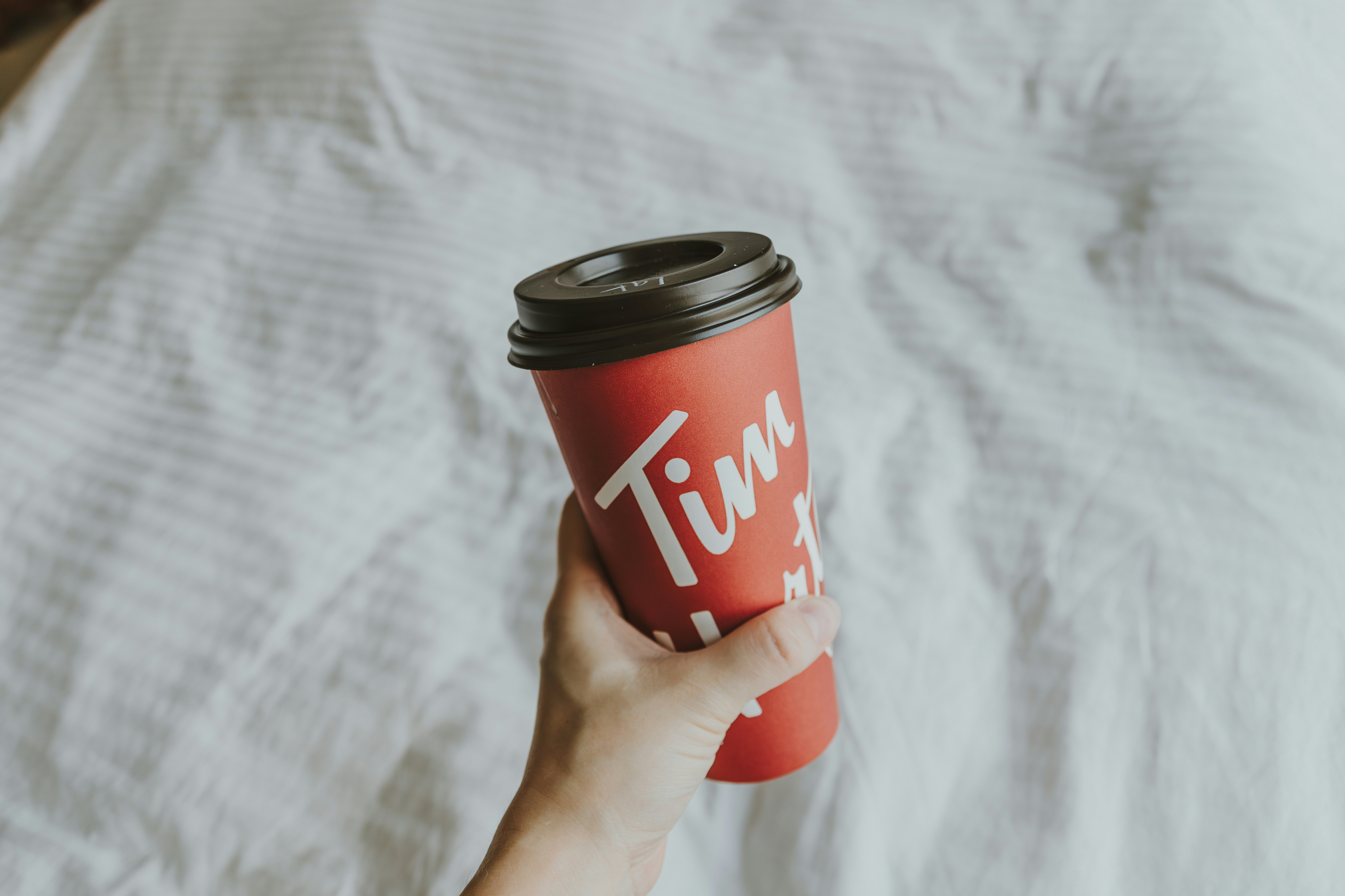 Seseorang memegang secangkir kopi di atas tempat tidur