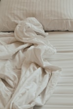 An unmade bed with white sheets and pillows