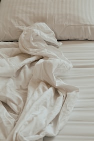 An unmade bed with white sheets and pillows